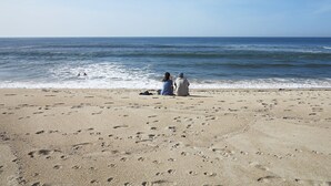A beach with footprints leading to the water, a couple sitting on the sand, and a person swimming.