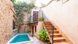 Une cour avec une piscine, des murs en pierre, un escalier et des plantes en pot.