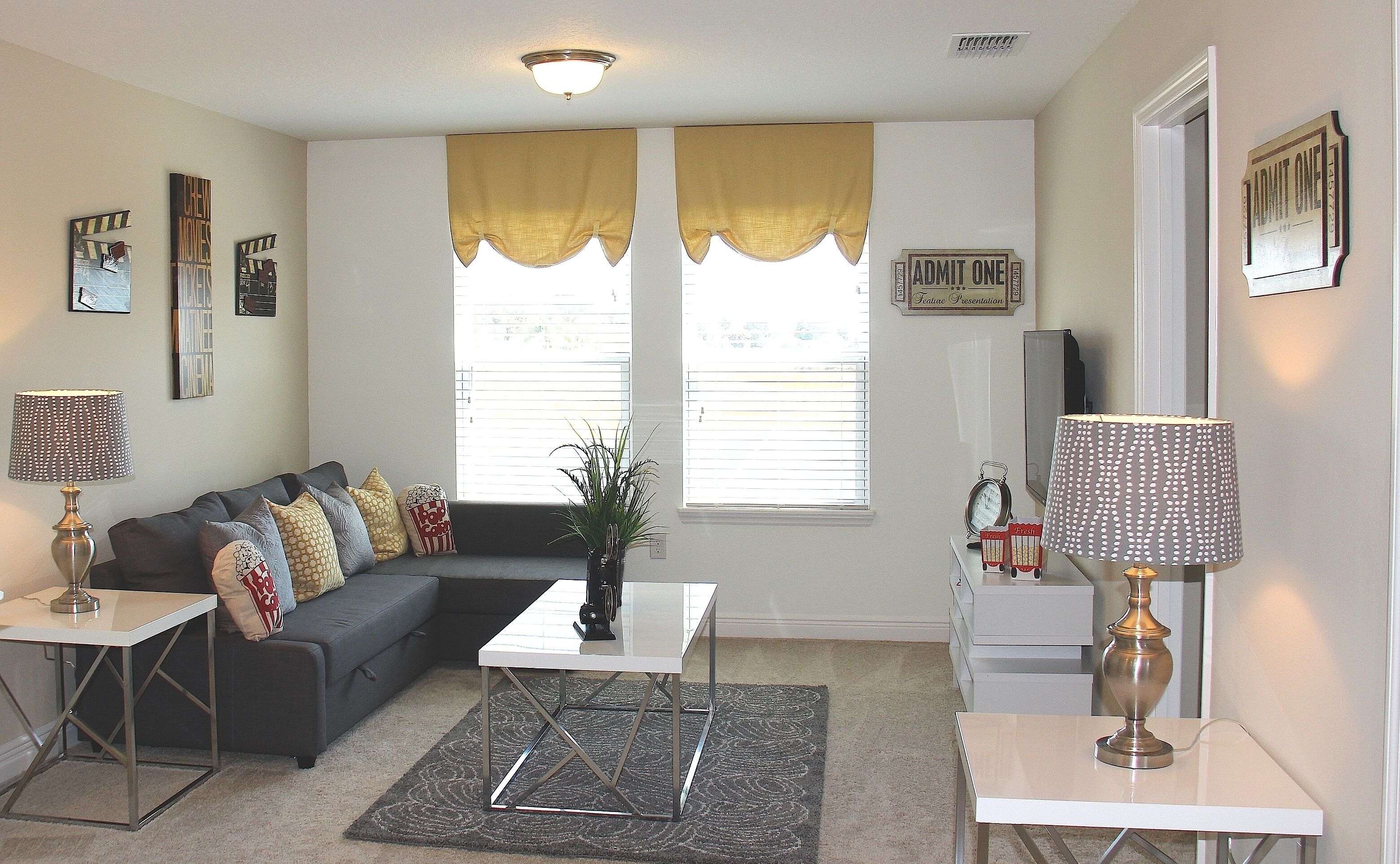 A living room with a sectional sofa, a coffee table, two lamps, a plant, and a window with curtains.