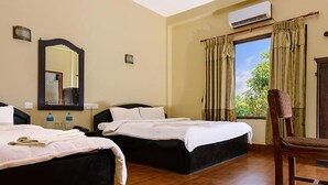 A hotel room with two beds, a wooden floor, a window with curtains, an air conditioning unit, and a chair. - Hotel Nature Heritage (Sauraha)