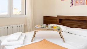 Una cama bien hecha con una bandeja de desayuno, una ventana con cortinas y un radiador.