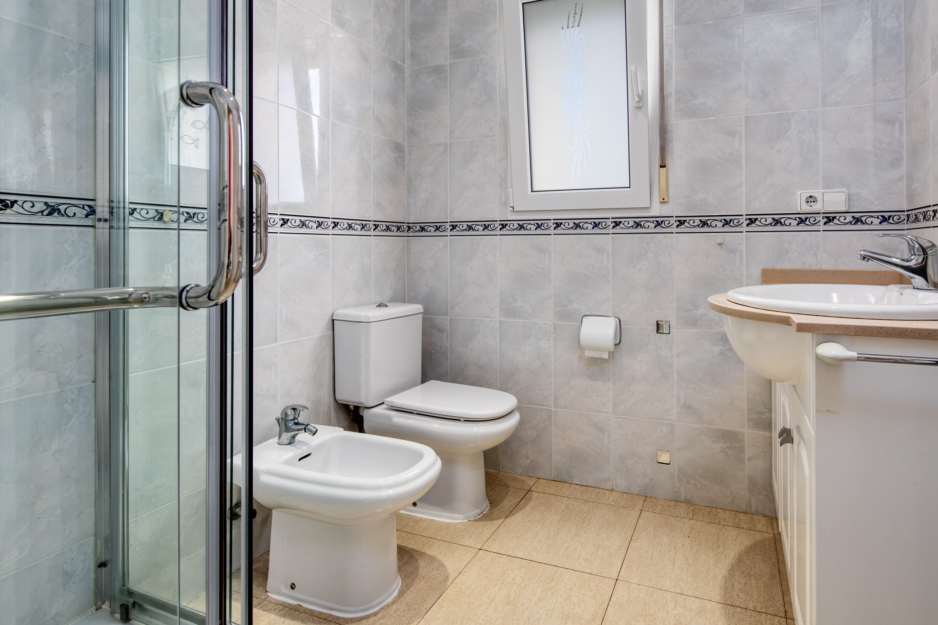 A bathroom with a glass shower enclosure, two toilets, a bidet, and a sink.