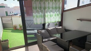 A patio area with wicker furniture, a glass table, and a view of a green lawn and parked cars.
