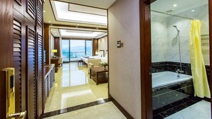 Habitación de hotel con balcón, cama grande, zona de estar y baño privado con ducha y bañera.