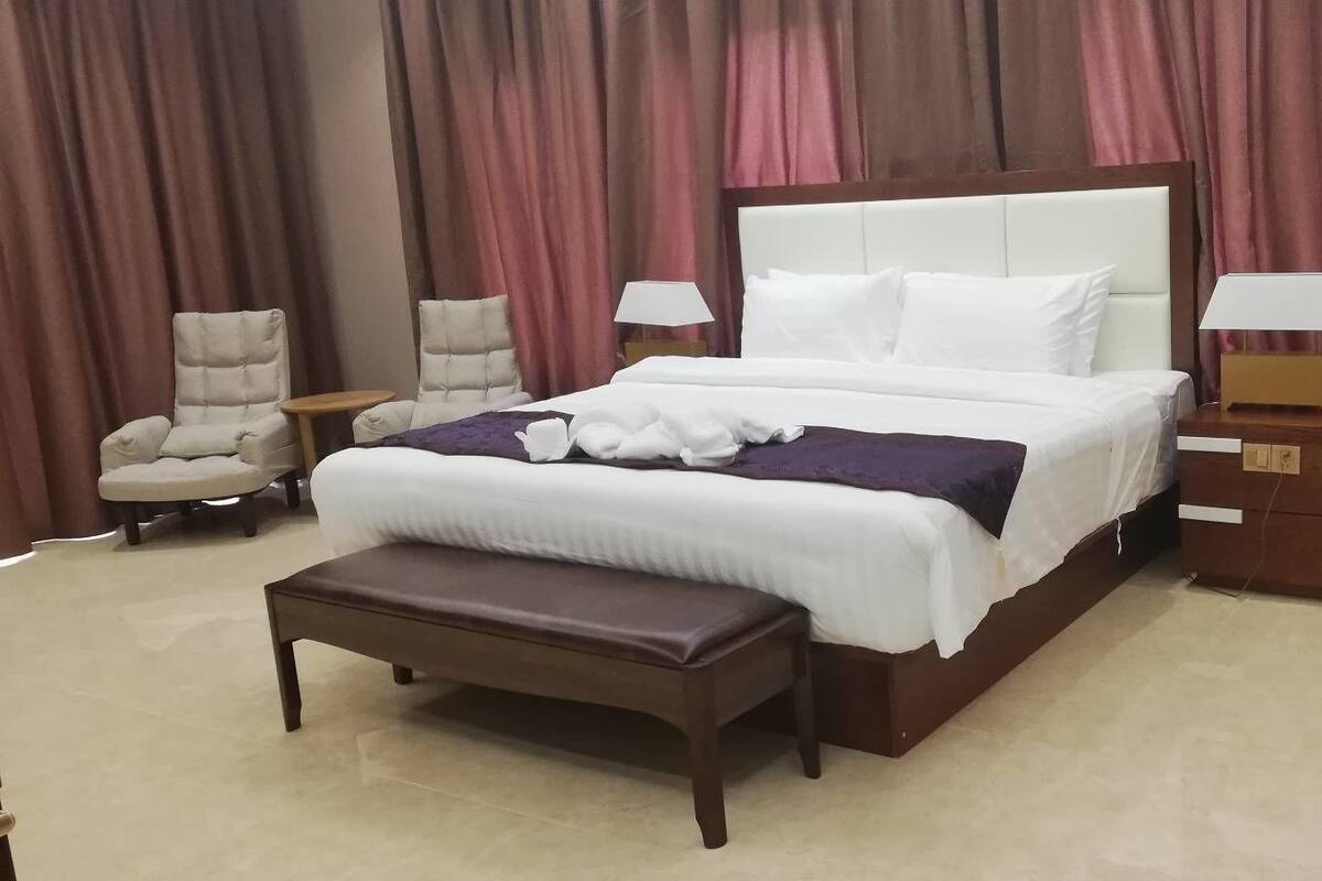 Quarto de hotel bem arrumado com uma cama grande, uma mesa de cabeceira, uma cadeira e um banco.