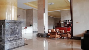 Un vestíbulo con columnas de mármol, un mostrador de recepción y una zona de estar con sillones y un sofá.