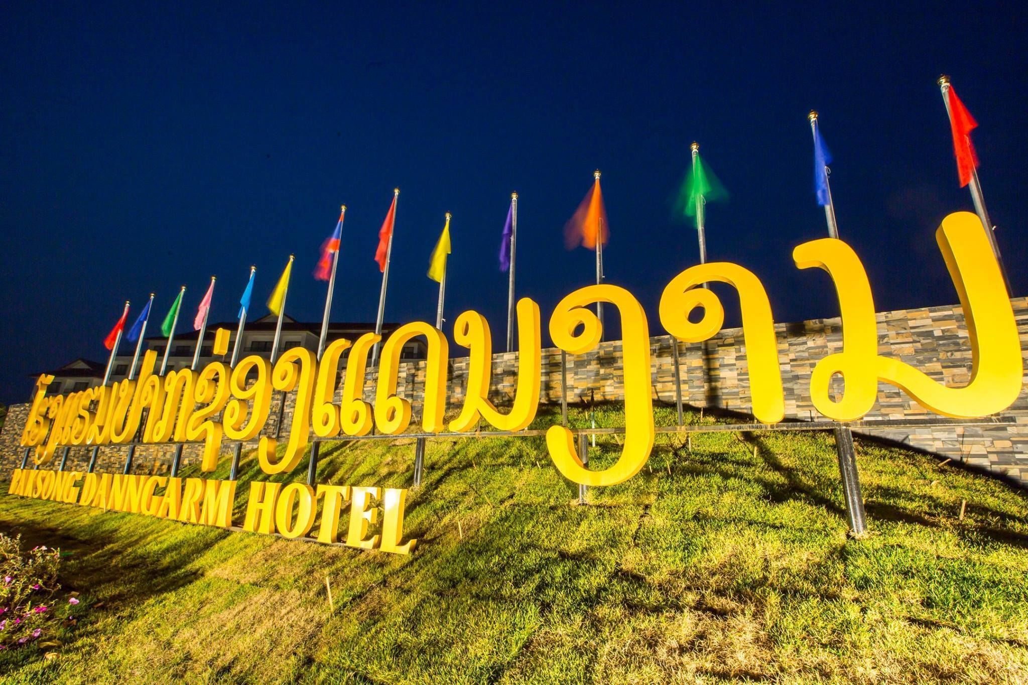 A hotel sign with multiple flags and the name "Taksong Danni CARM HOTEL" in large yellow letters.