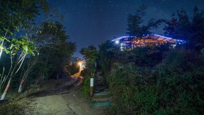 A starry night sky, a dirt path leading to a building with a roof structure, surrounded by greenery. - LaHermitage Resort (Lansdowne)