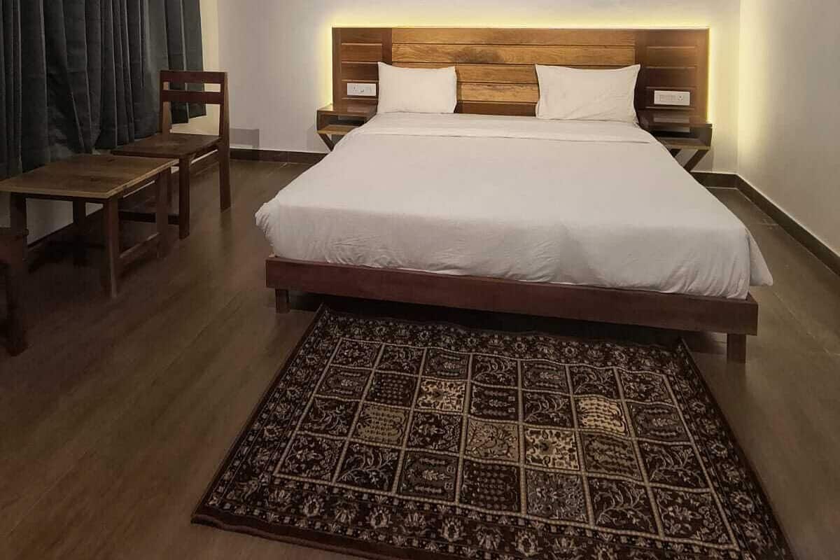 A bedroom with a bed, wooden headboard, bedside tables, a chair, a patterned rug, and a ceiling fan.