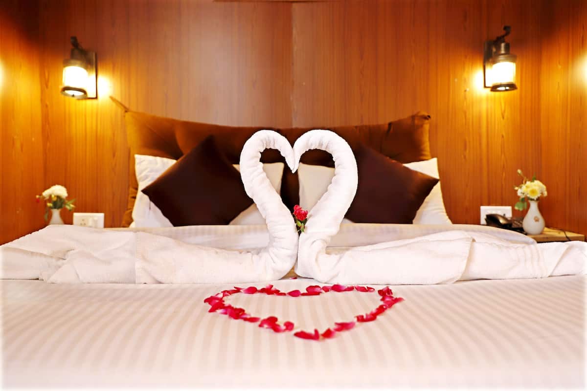 A hotel room with a bed, pillows, a heart-shaped arrangement of towels, and a heart-shaped arrangement of rose petals.