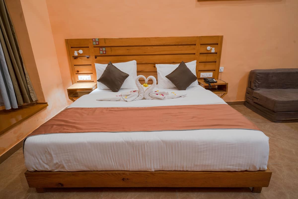 A neatly made bed with a wooden headboard, a bedside table with a lamp, and a grey sofa.