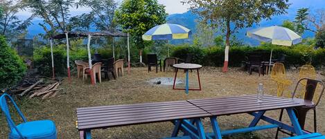 An outdoor seating area with tables and chairs, surrounded by trees and a view of mountains.