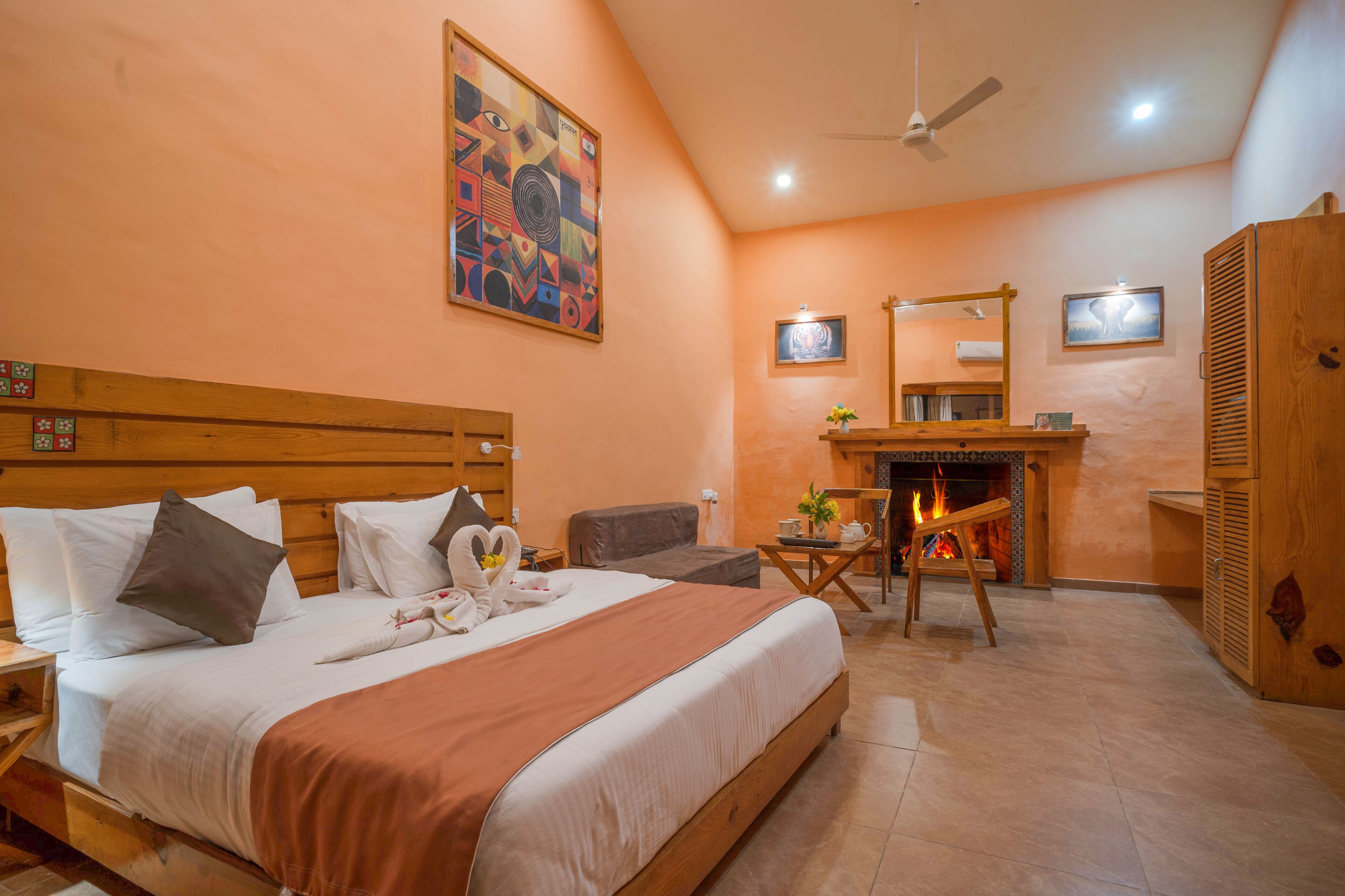 A hotel room with a large bed, a wooden headboard, a fireplace, a ceiling fan, and a painting on the wall.