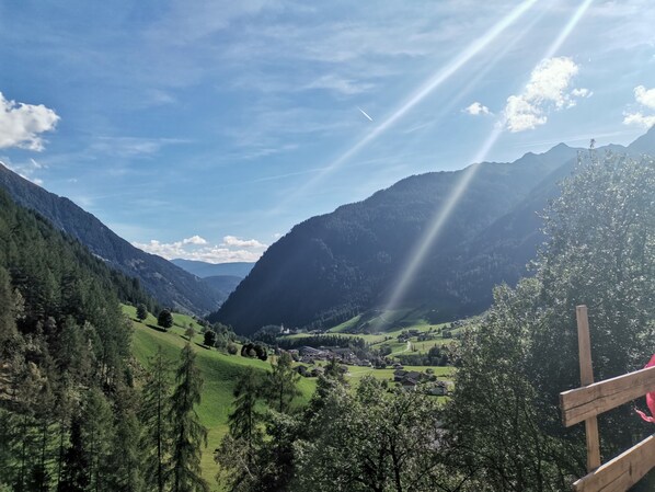 Un paysage montagneux avec une vallée, des maisons et une structure en bois au premier plan.