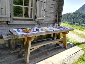 Une table en bois rustique, installée à l’extérieur, offre une vue sur une montagne boisée en arrière-plan.