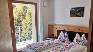A bedroom with a wooden bed, floral bedding, a view of trees through a window, and a painting on the wall. - Beautiful chalet - The mountains on the doorstep  (Vintl/Pfunders)