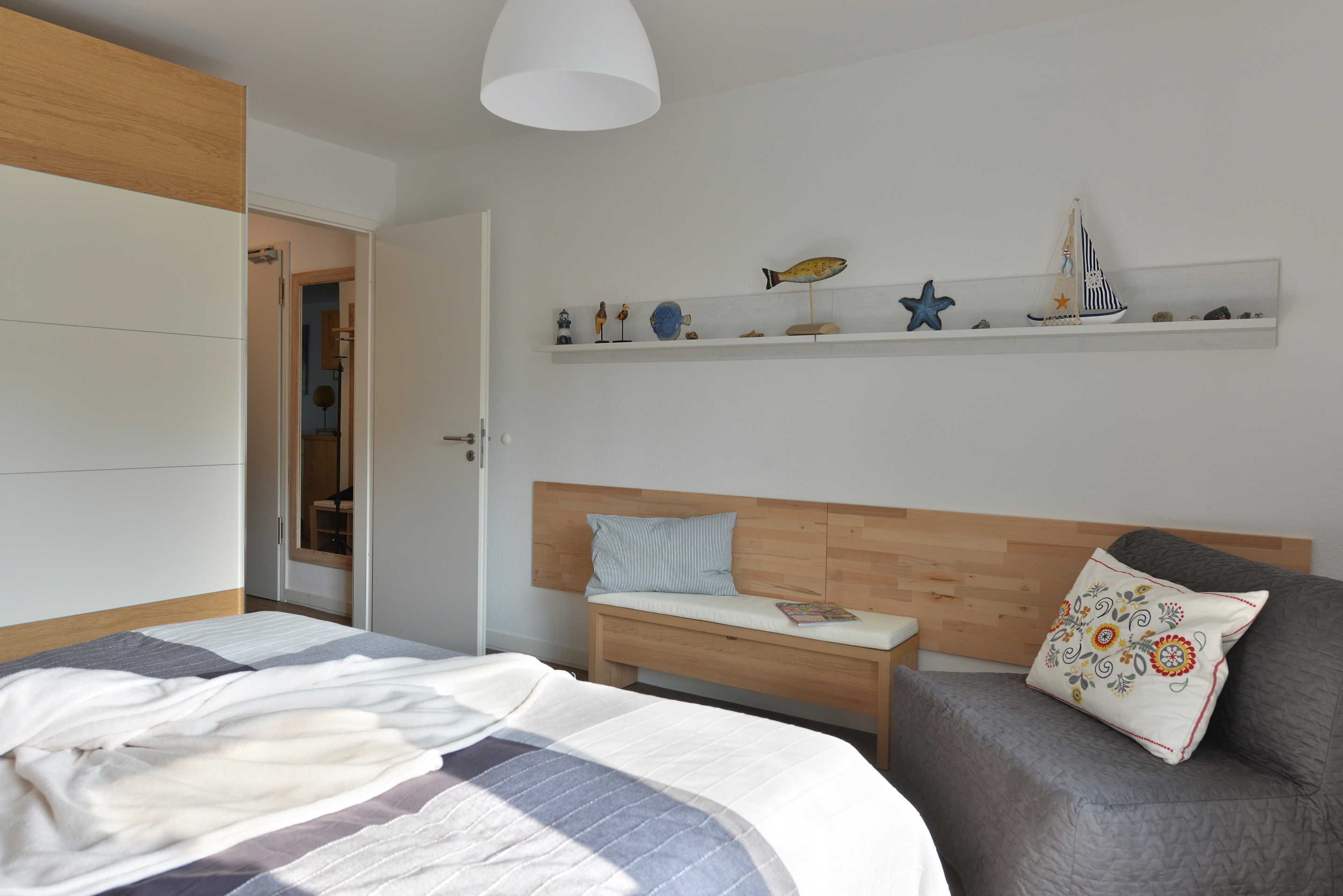 A bedroom with a bed, a bedside table, a bench, a wardrobe, and a shelf with decorative items.