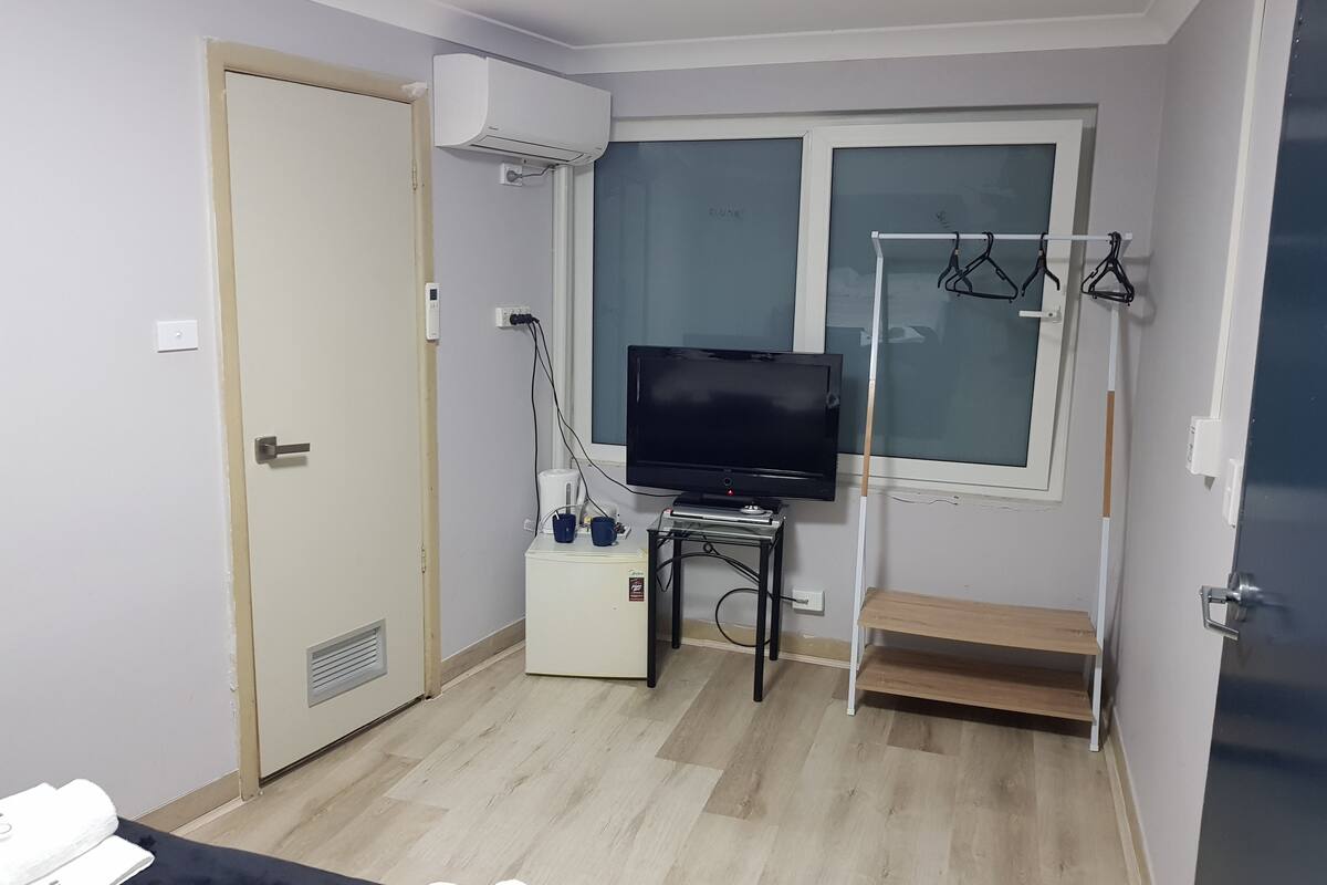 A small, well-lit room with a television, a heater, and a window with a view.
