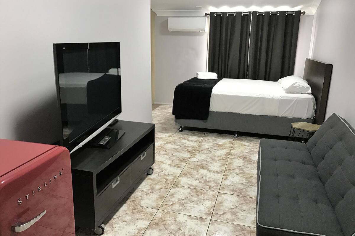 A hotel room with a bed, a TV, a sofa, and a red suitcase.