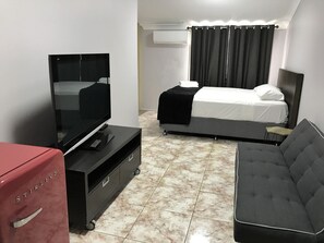Una habitación de hotel con una cama, un televisor, un sofá y una maleta roja.