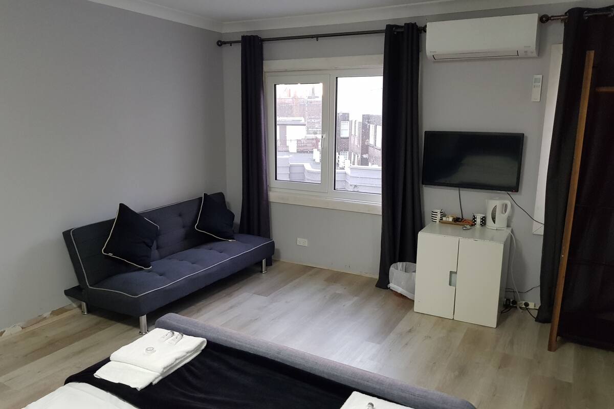 A modern hotel room with a sofa, a bed, a TV, and a window with curtains.