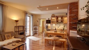 Ein gemütliches Wohnzimmer mit Holzboden, einer Couch, einem Couchtisch und einem Essbereich mit Tisch und Stühlen. Es gibt eine Küche mit Holzausstattung und einer Ziegelwand.