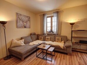 A cozy living room with a brown leather sofa, a glass coffee table, and a painting of a deer on the wall.