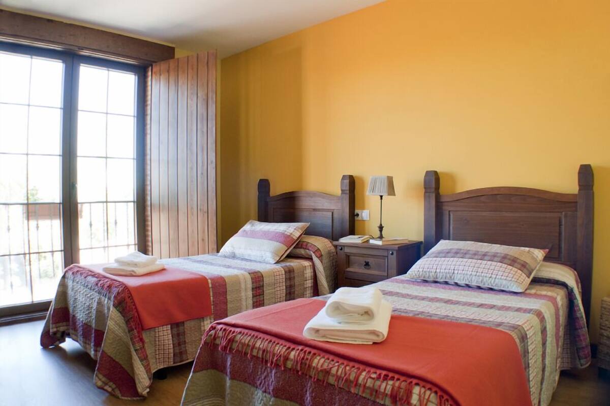 A hotel room with two beds, a window, and a nightstand with a lamp.