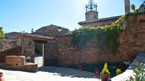 Un patio con muros de piedra, una reja y plantas en macetas.