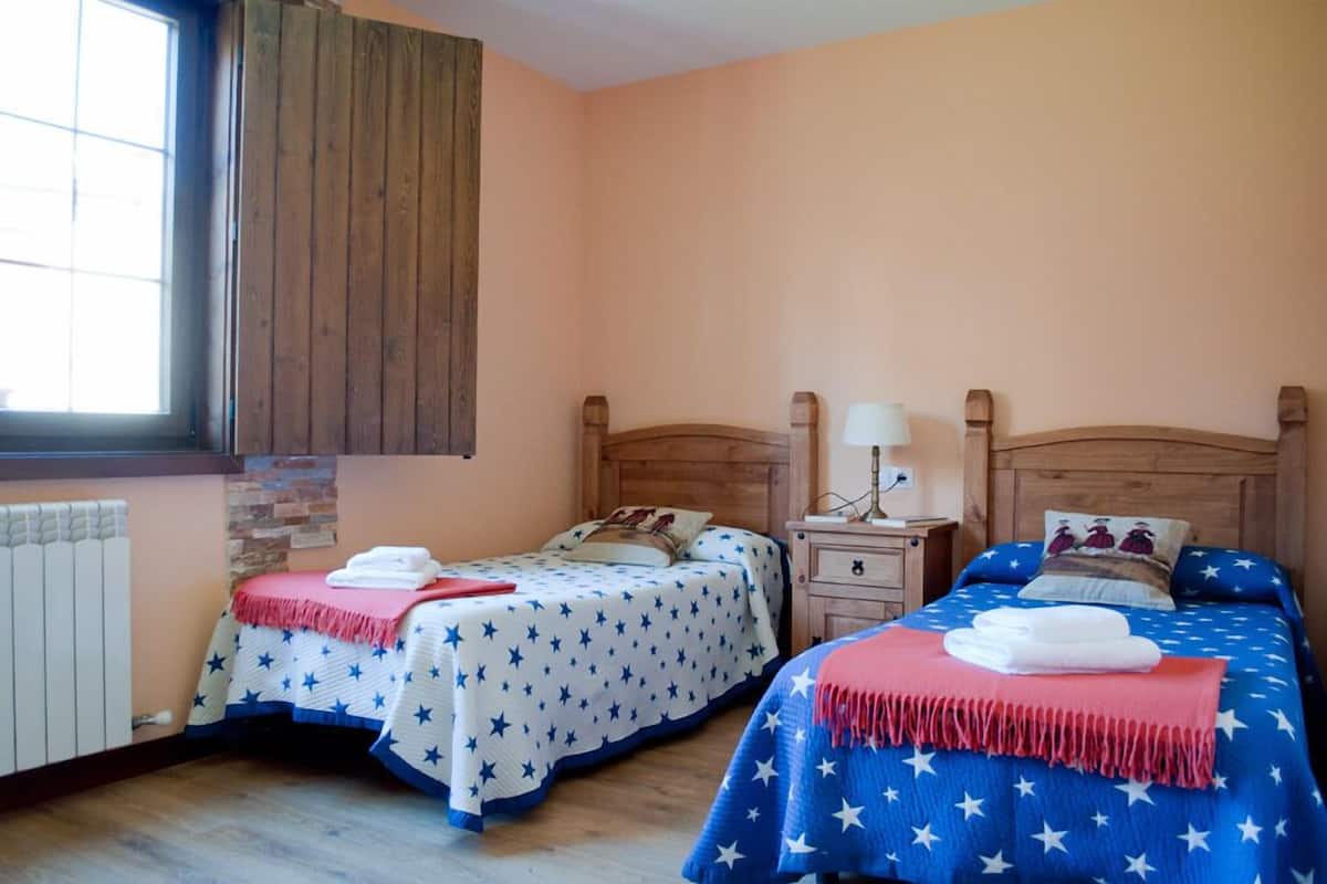 A room with two beds, each with a star-patterned bedspread, a wooden headboard, and a nightstand with a lamp.
