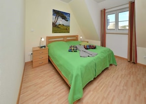 Une chambre à coucher avec un lit, une table de chevet, une lampe, une fenêtre avec des rideaux et un tableau au mur.