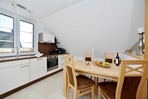 A modern kitchen with white cabinets, a wooden dining table, and a window with blinds.