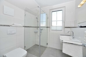 Ein modernes Badezimmer mit einer einachig abgetrennten Dusche, einem weißen Waschbecken und einem Fenster für natürliches Licht.