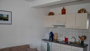 A compact kitchen with white cabinets, a small refrigerator, and a sink. - Apartment 1 - Apartments Meyer (Bollewick)