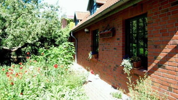 A brick house with a sloped roof, a small porch, and a garden with flowers. - Apartment 1 - Apartments Meyer (Bollewick)