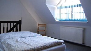 A bedroom with a sloped ceiling, a single bed, a chair, and a window with blue blinds. - Apartment 1 - Apartments Meyer (Bollewick)