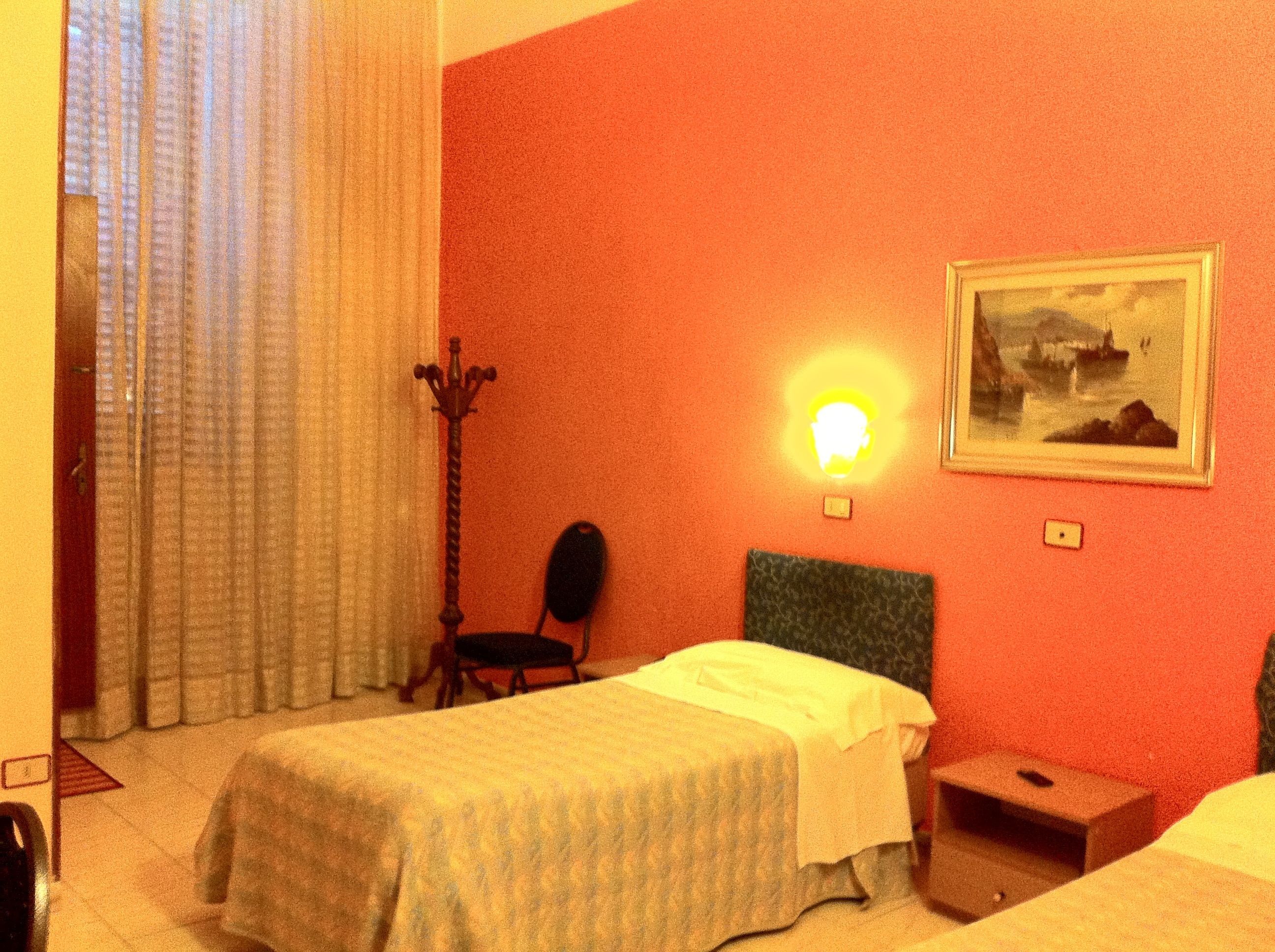 Une chambre d’hôtel avec un lit, une chaise, une table de chevet, une lampe et un tableau au mur.