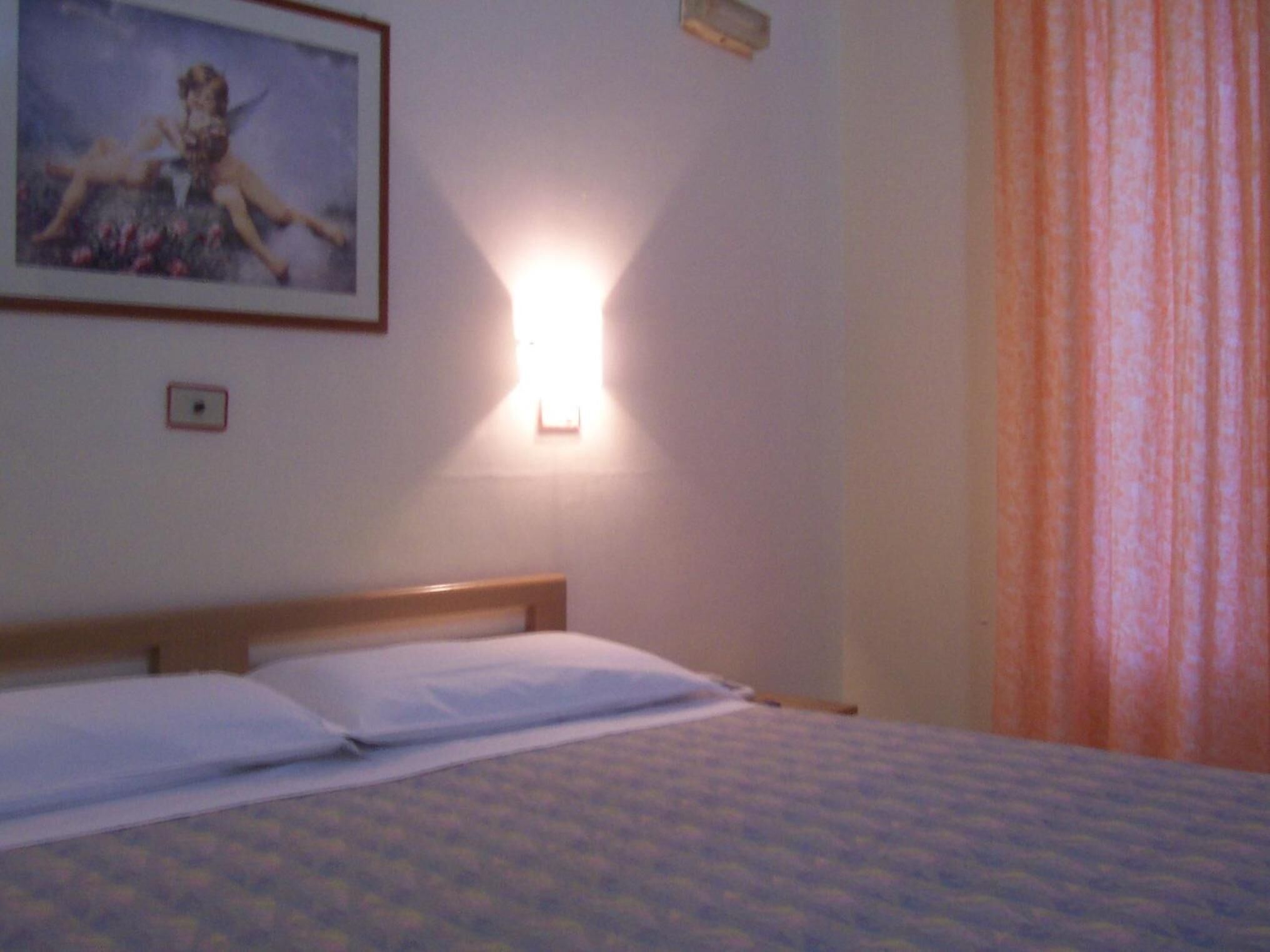 Une chambre d’hôtel avec un lit, une lampe fixée au mur et un tableau encadré.