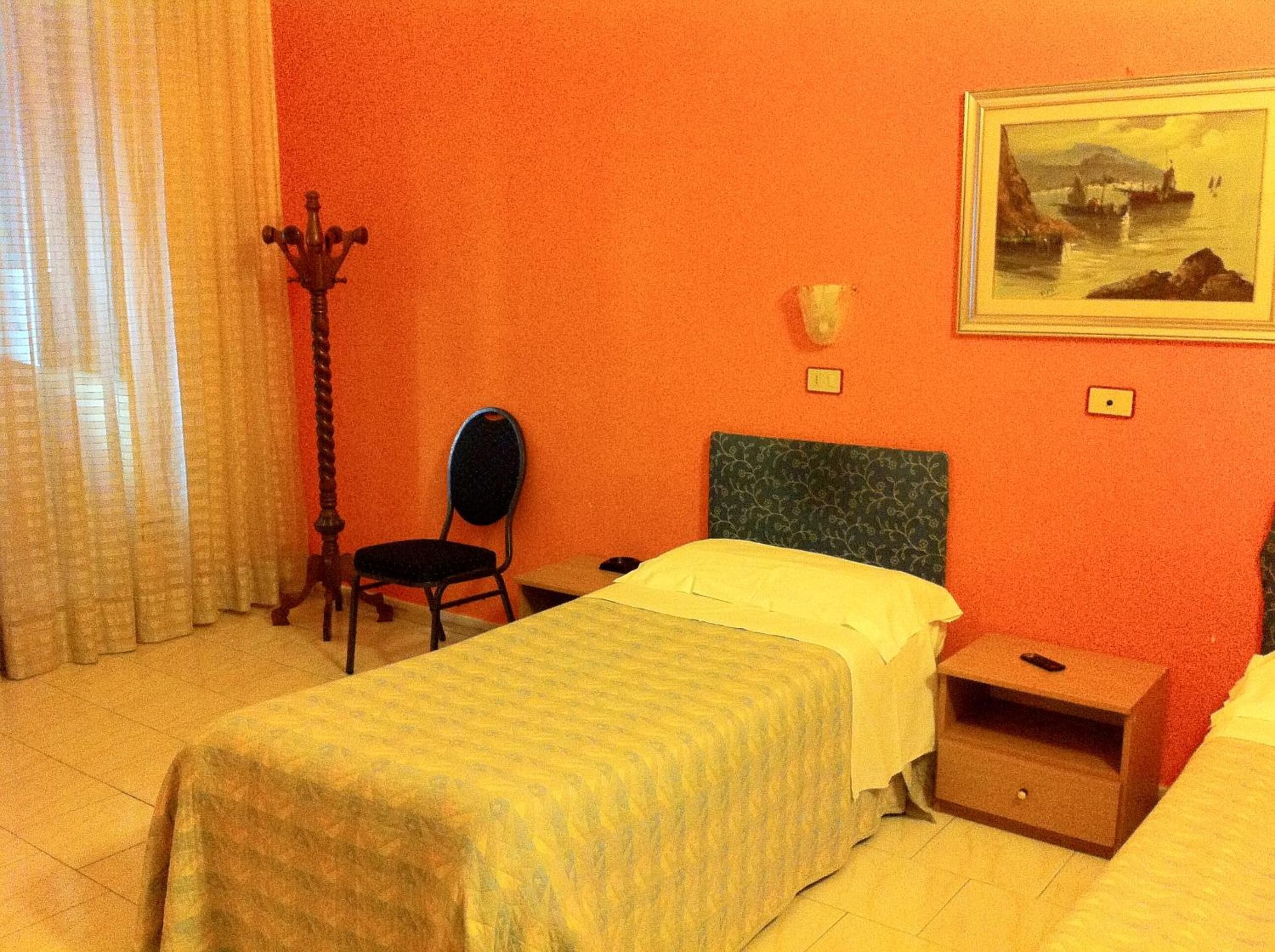 A room with a bed, a chair, a nightstand, and a painting on the wall.