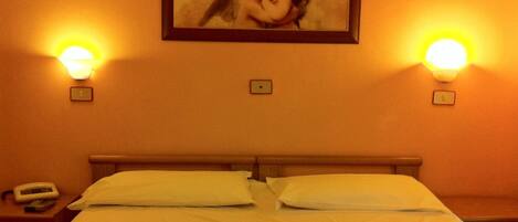 A hotel room with a bed, two bedside lamps, a painting on the wall, and a phone on the nightstand.
