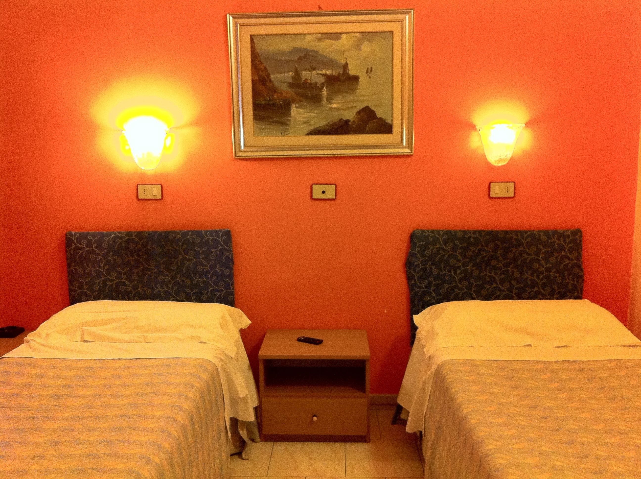 A hotel room with two beds, a nightstand, and a painting on the wall.