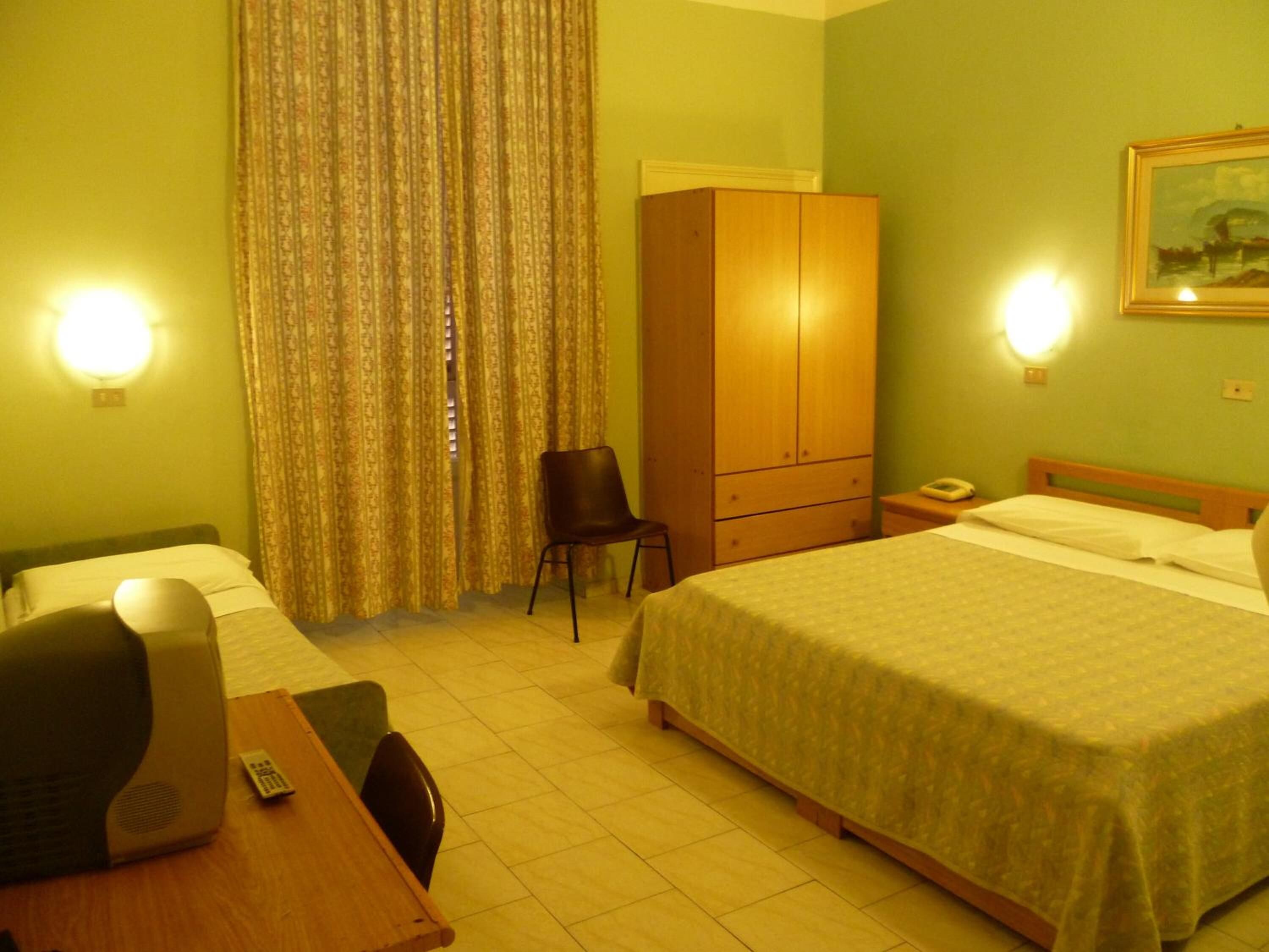 A hotel room with two beds, a desk with a computer, a chair, a wardrobe, and a painting on the wall.