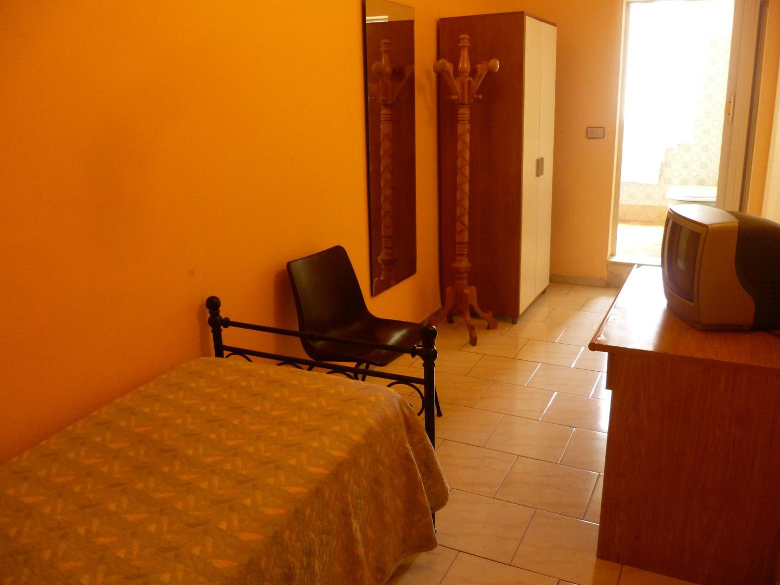 Un dormitorio con cama, una silla, un televisor y un armario.