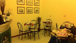 A dining area with metal chairs and tables, a coffee machine, and framed pictures on the wall.