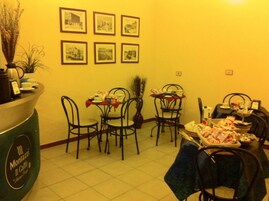Zona pranzo con sedie e tavoli in metallo, una macchina da caffè e quadri appesi alle pareti.