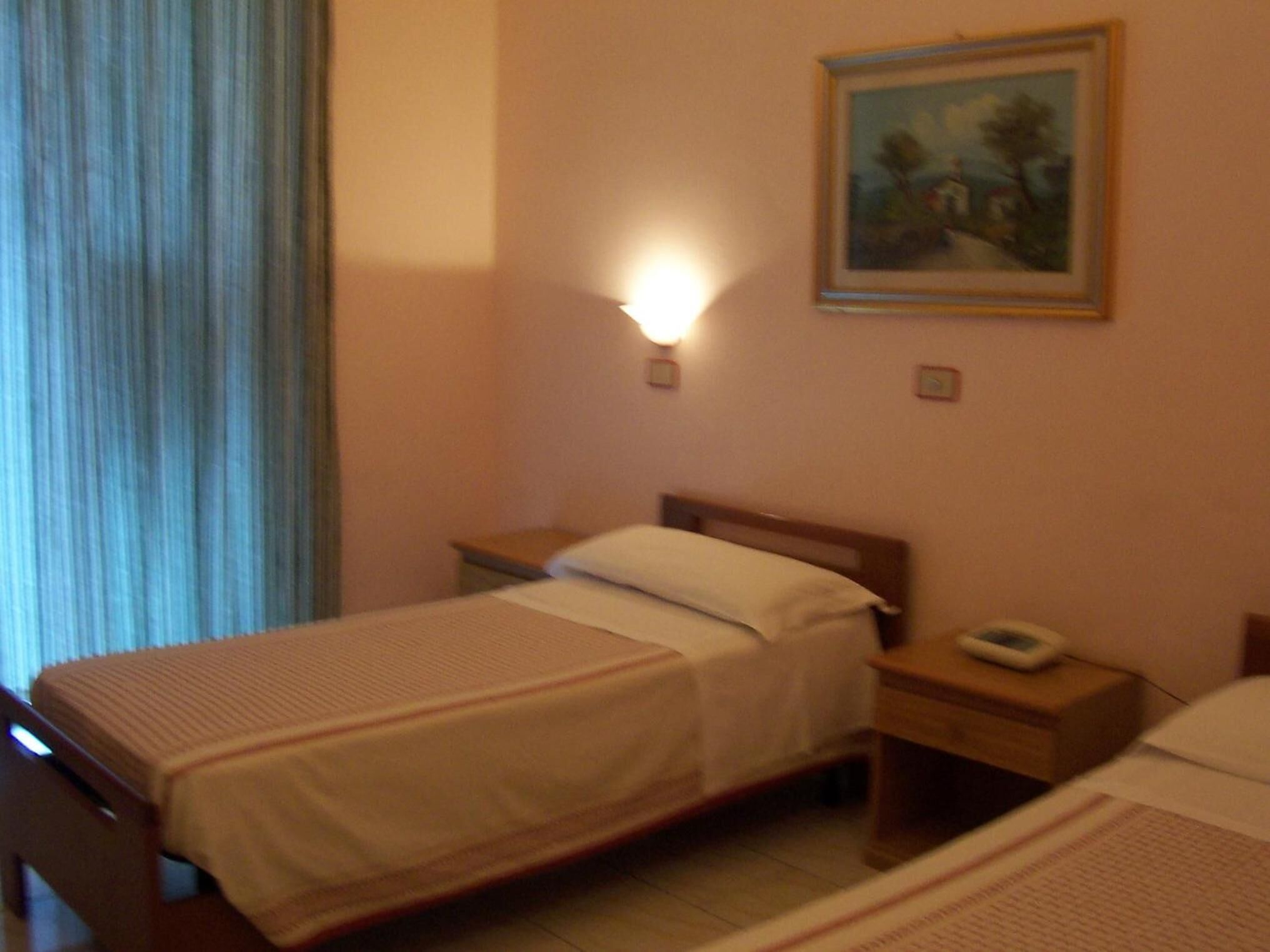 A hotel room with a bed, bedside table, and a painting on the wall.