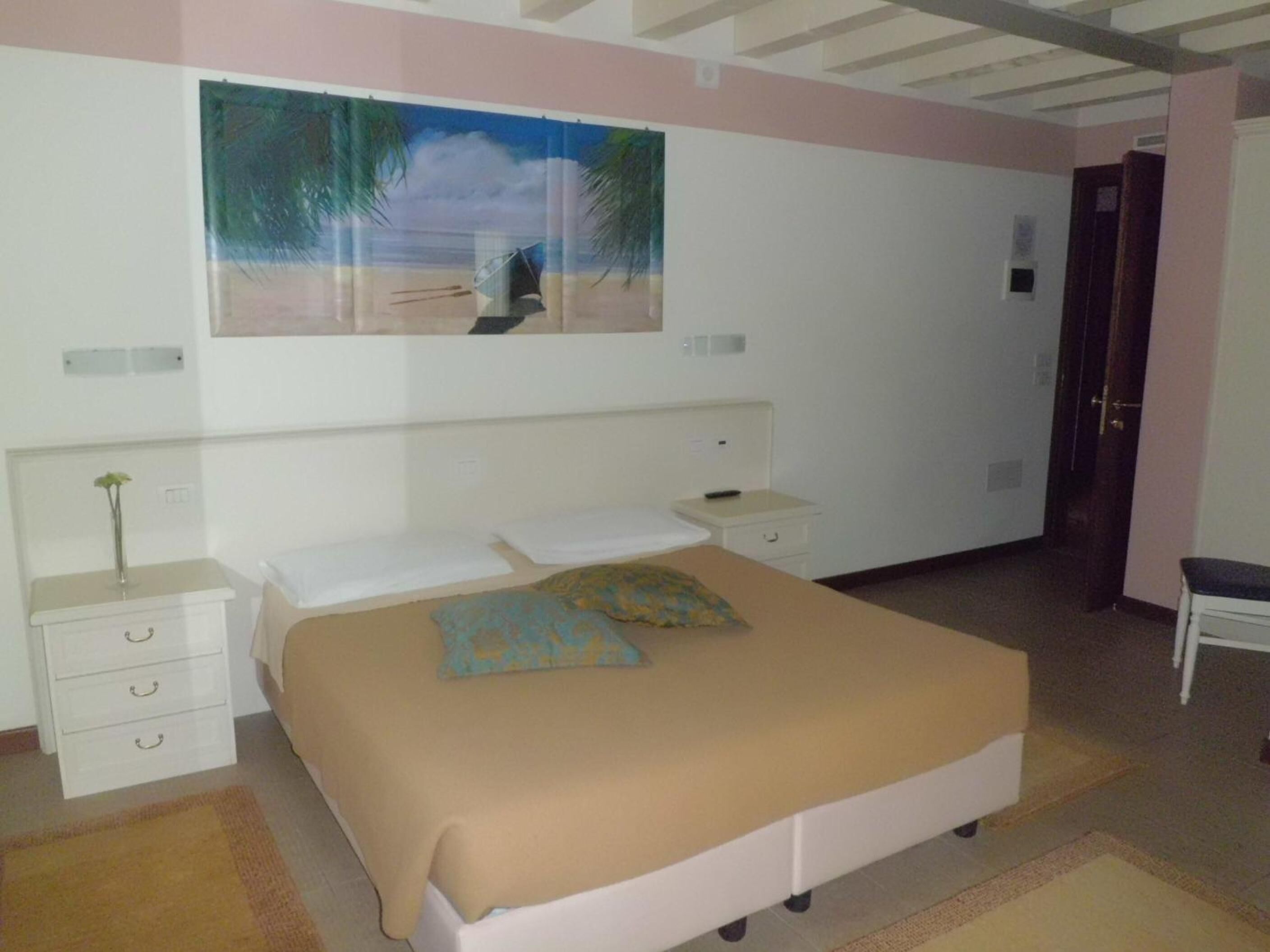 Un dormitorio con una cama, una mesita de noche, un armario con cajones, un cuadro y una puerta.