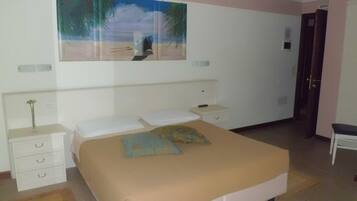 Un dormitorio con una cama, una mesita de noche, un armario con cajones, un cuadro y una puerta.