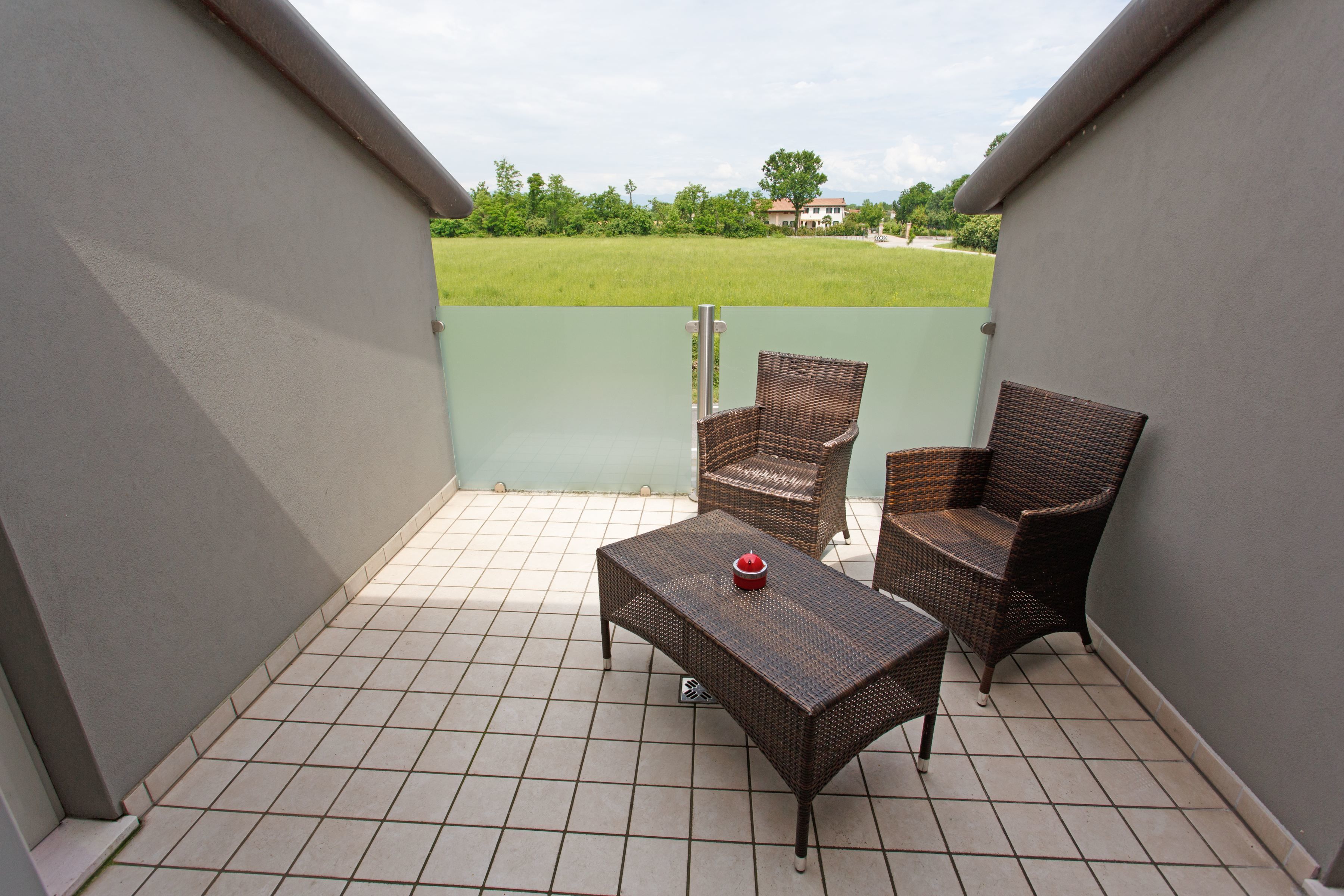 Un balcon doté d’un sol carrelé, de deux fauteuils en osier et d’une petite table sur laquelle se trouve un objet rouge.
