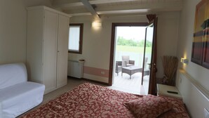A bedroom with a bed, a wardrobe, a small table with a remote control, and a view of an outdoor patio with chairs. - Sweet Home (Treviso)